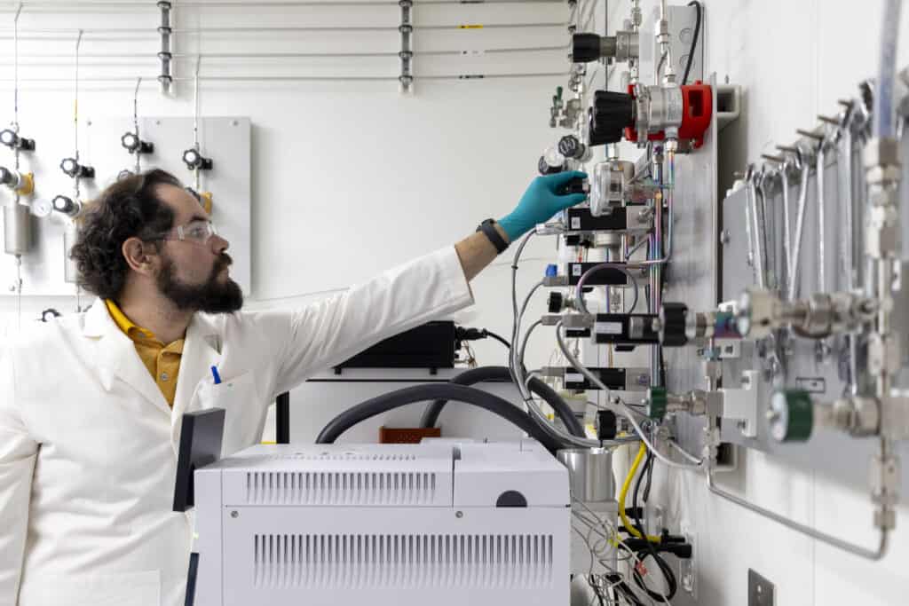 A man in a lab coat checks on a gauge used in a science experiment.