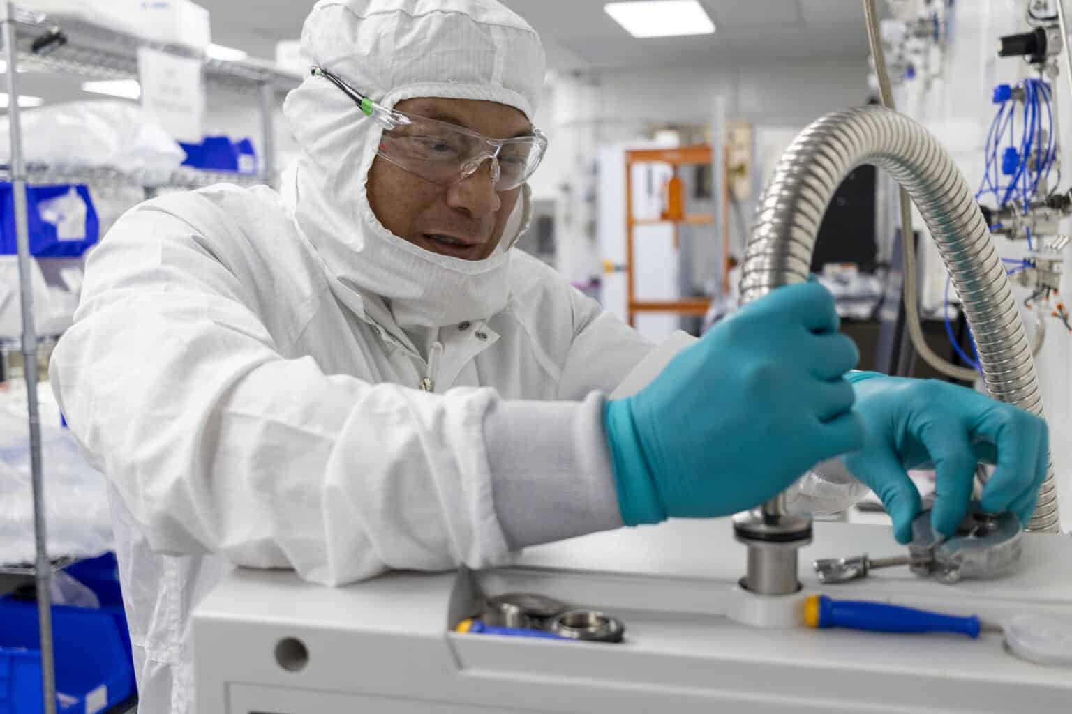 Person in a white clean suit working with tools and machinery at a table in a clean room