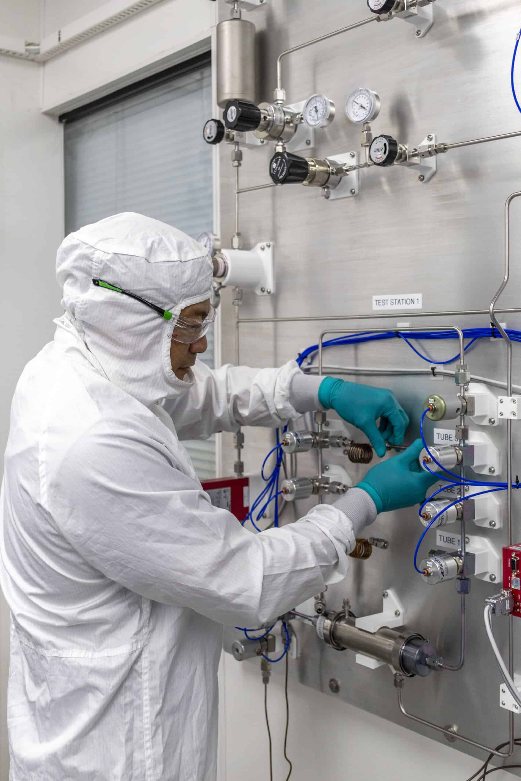 A person in a white clean suit adjusting controls on a clean room.