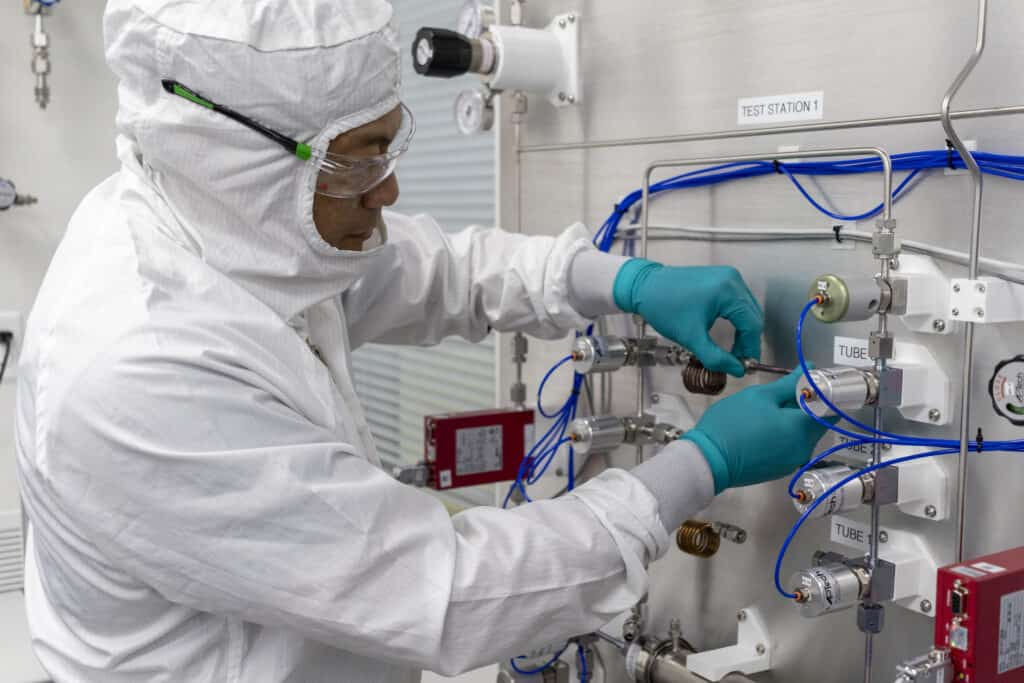 A person in a white clean suit adjusting controls on a clean room.