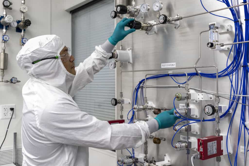 A person in a white clean suit adjusting controls on a clean room.