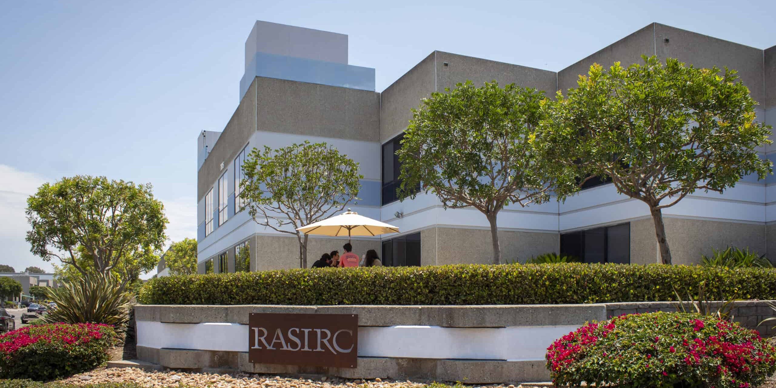 The exterior of a tan colored office building landscaped with trees and plants.