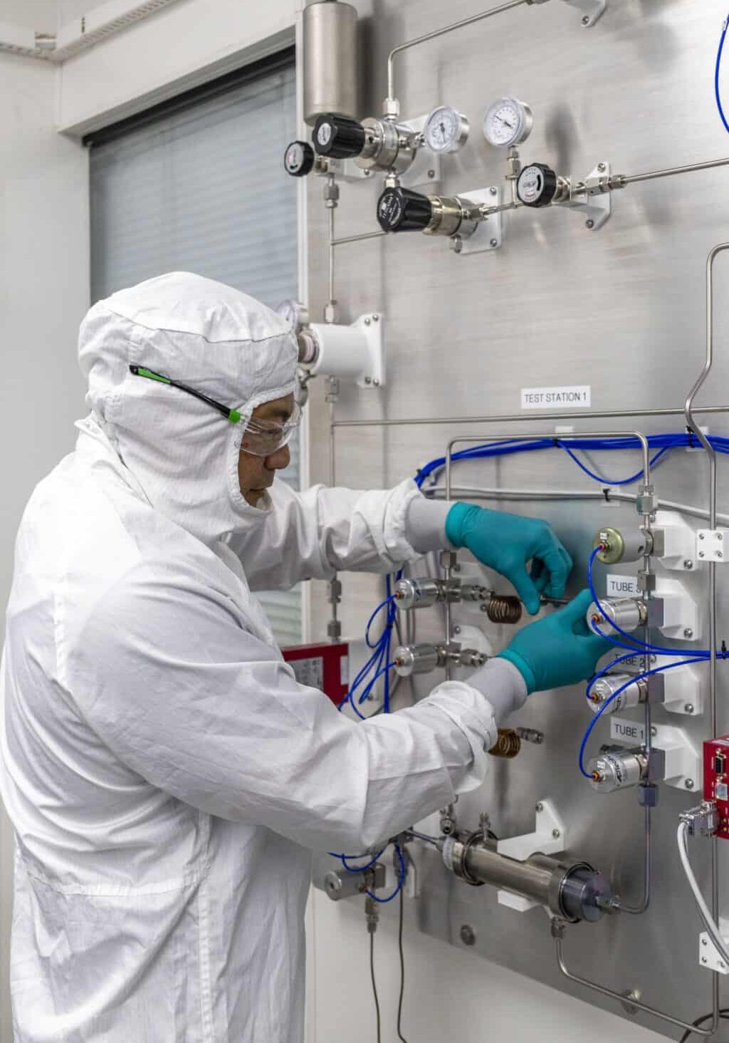 A person in a white clean suit adjusting controls on a clean room.